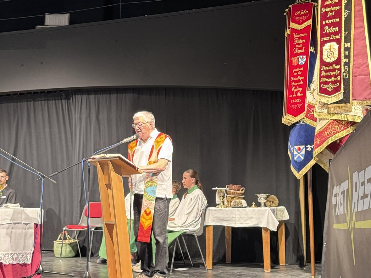 Pfarrer Kahnert zelebriert den Gottesdienst im Rahmen des Brunnenfestes im Theaterstadel Heinrichshofen.  Ministranten sind im Hintergrund. Seitlich sind die Fahen der Vereine.