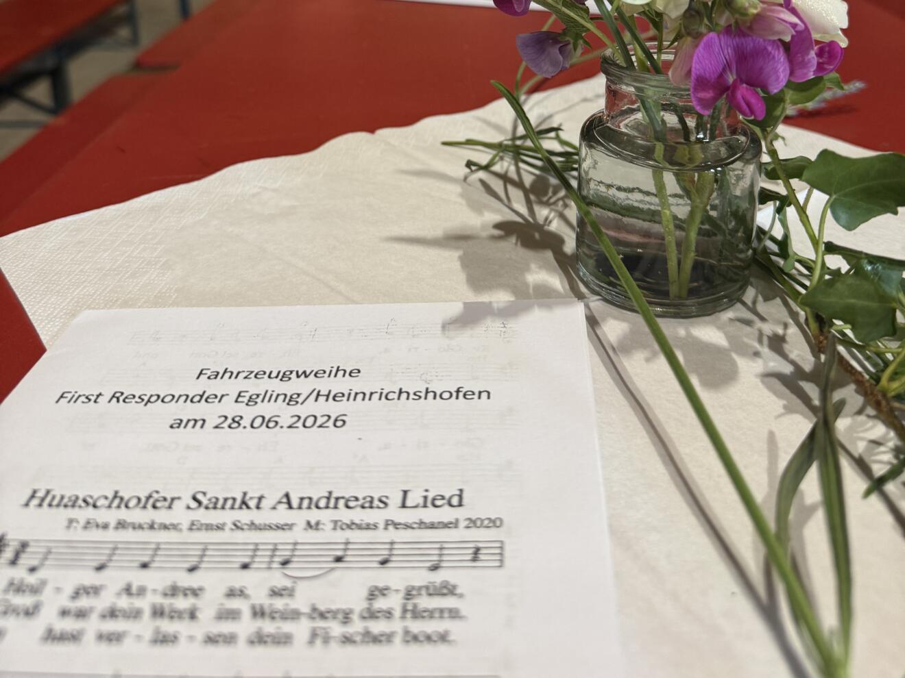 Es ist ein festlicher Tisch mit Blumenschmuck und Liedblatt für den Gottesdienst zu sehen